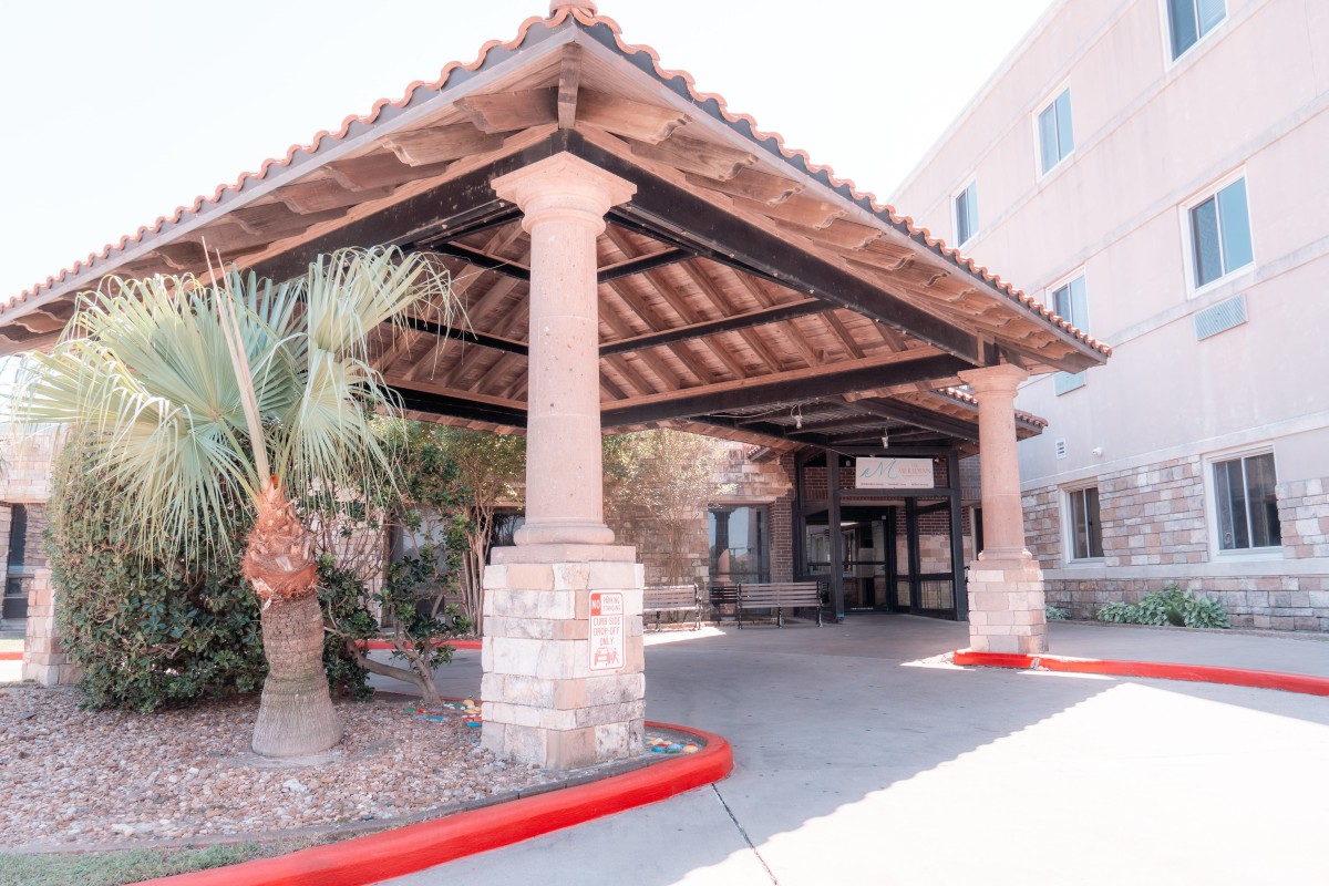 Entrance with a covered canopy supported by columns and a nearby palm tree.
