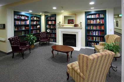 A cozy library room featuring bookshelves, a fireplace, and comfortable seating.