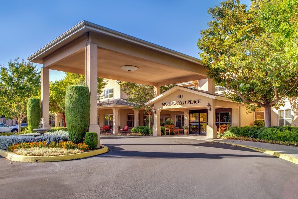 The exterior entrance of a hotel, featuring a covered driveway and landscaped greenery.