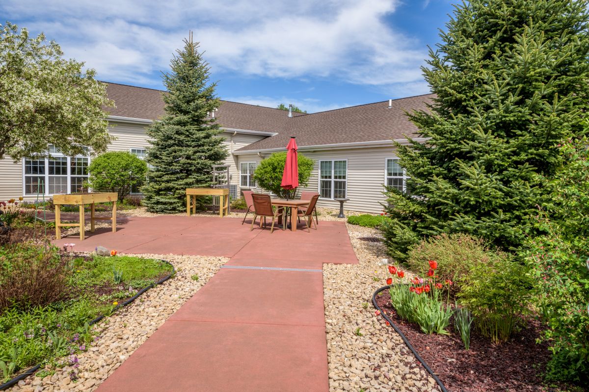 A landscaped outdoor patio area with a red umbrella, surrounded by greenery and trees.