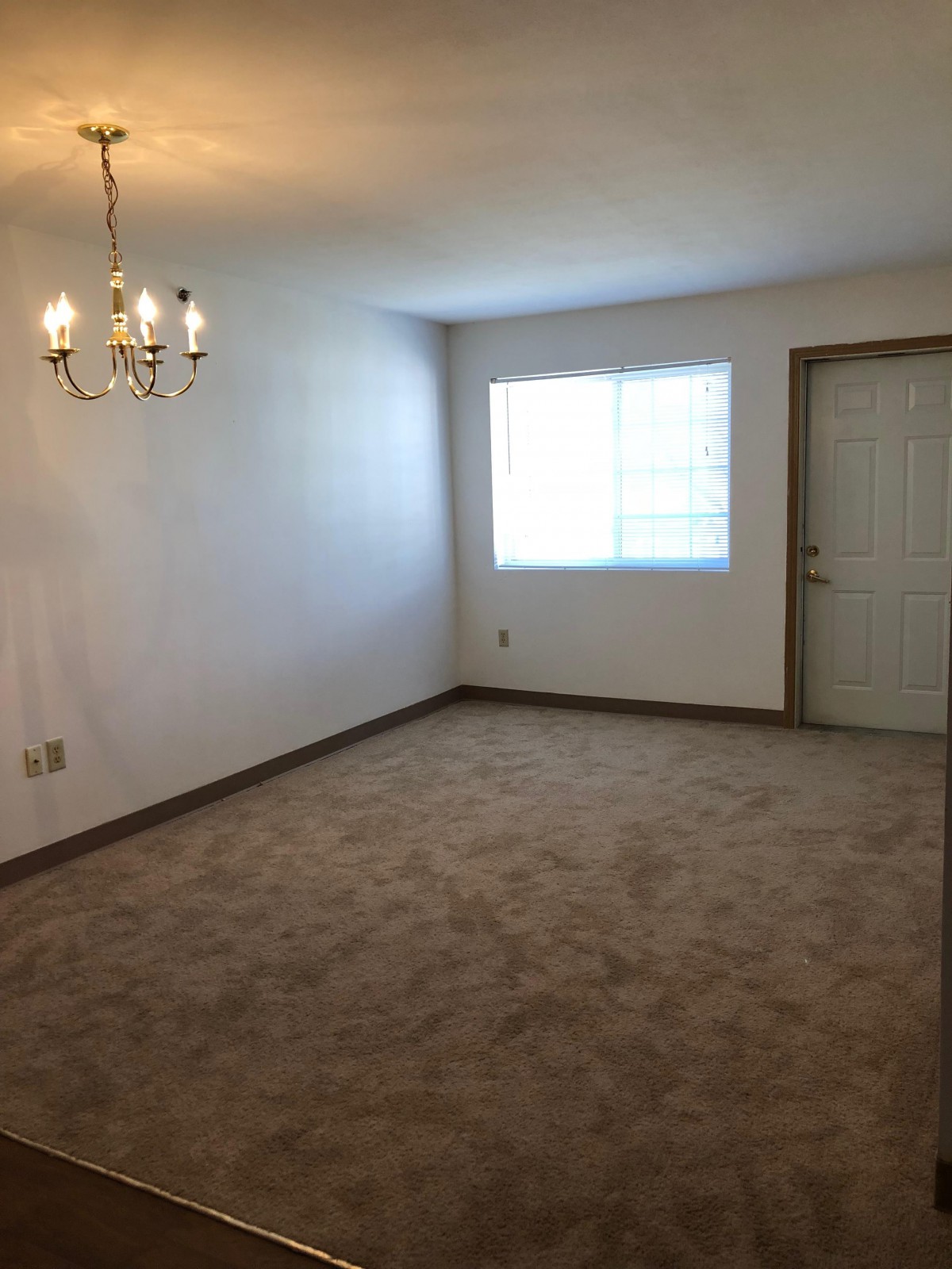 An empty room with carpet flooring, a chandelier, a window, and a door.