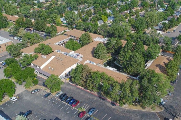 Aerial view of a building surrounded by trees with a parking lot in the foreground.