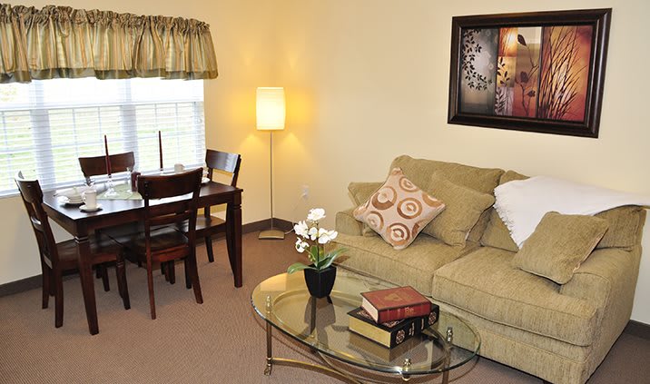 A cozy living room with a sofa, coffee table, dining area, and warm lighting.