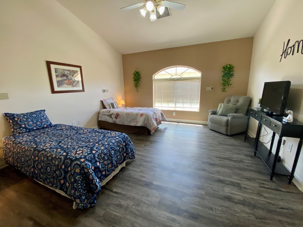 A spacious bedroom with two beds, wood flooring, and a cozy armchair by the window.