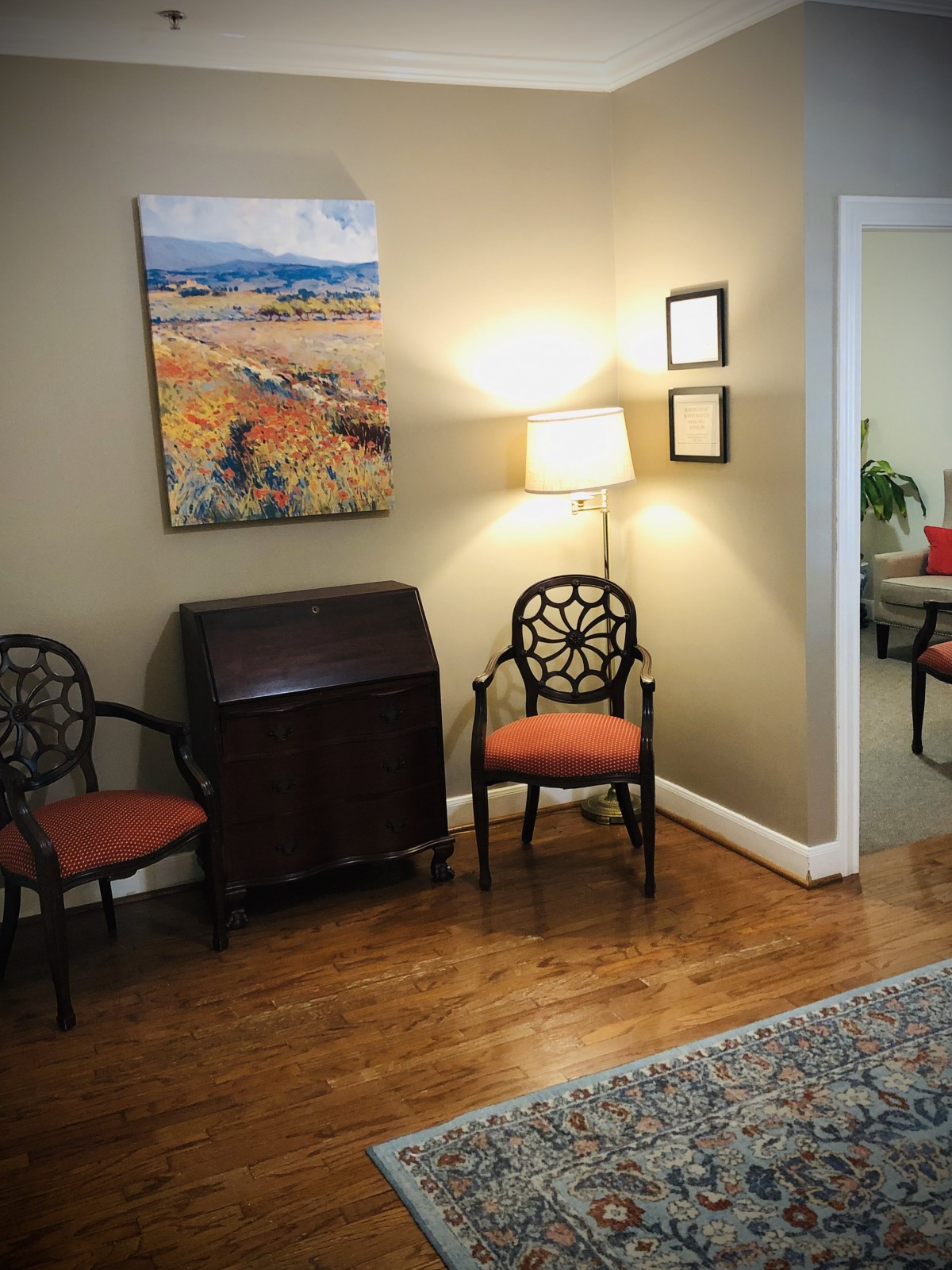 A cozy living room corner with two chairs, a lamp, and a colorful painting on the wall.