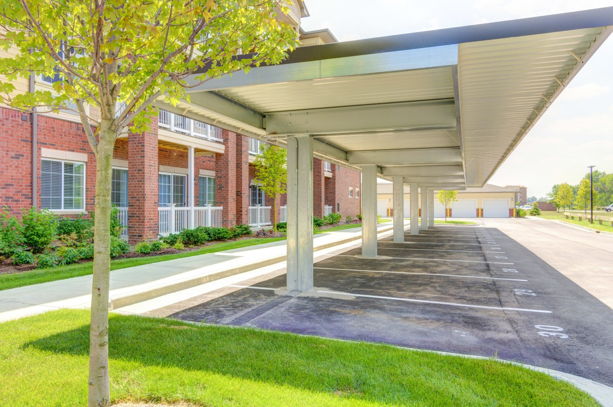 Covered parking area outside an apartment complex with trees and green landscaping.
