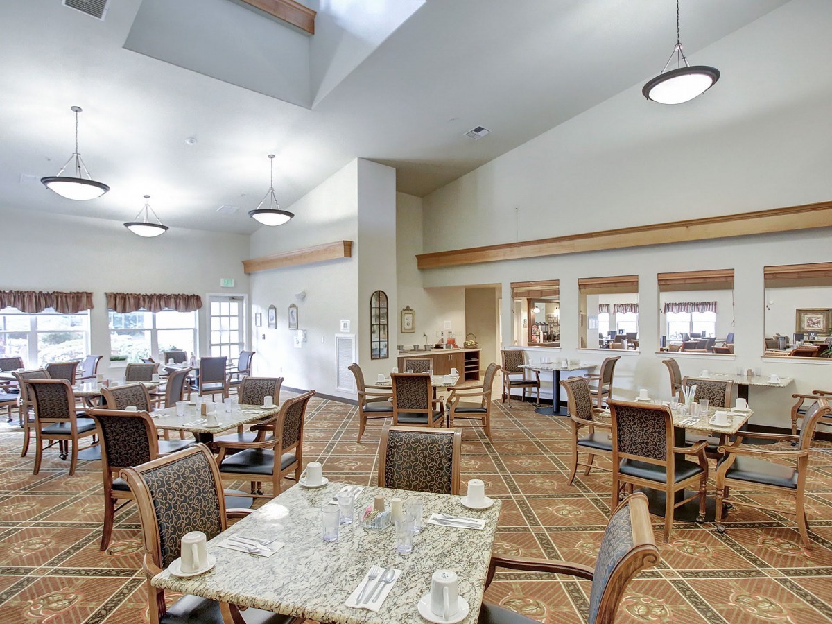 A spacious and well-lit dining area featuring multiple tables and chairs, with a carpeted floor and modern interior design.