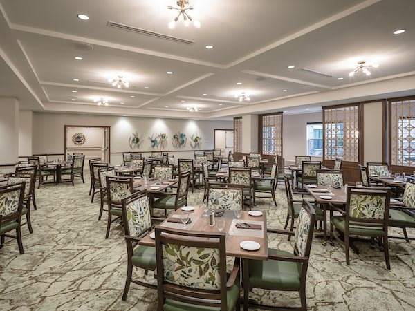 A well-lit and elegantly designed dining area with multiple tables and chairs, featuring chandeliers and decorative elements.