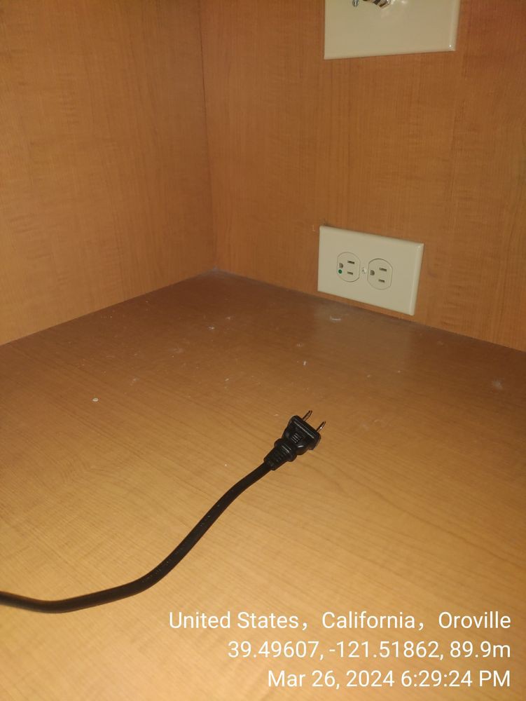 A lone power cord lies disconnected on a wooden surface, near an electrical outlet.