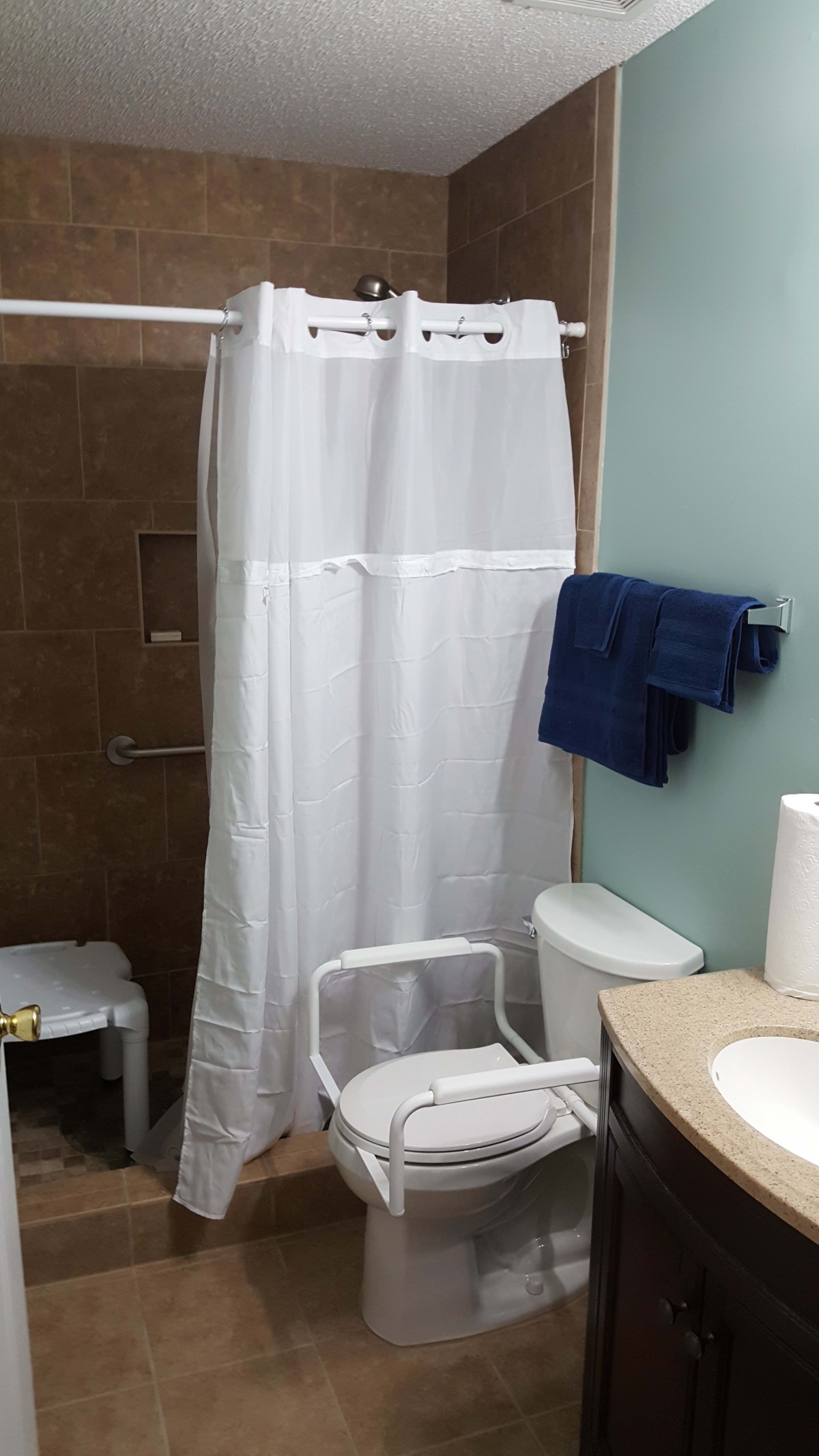 An accessible bathroom setup with a shower curtain, toilet with grab bars, and towels.