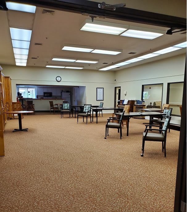 A spacious, empty office room with chairs and tables arranged on a carpeted floor.