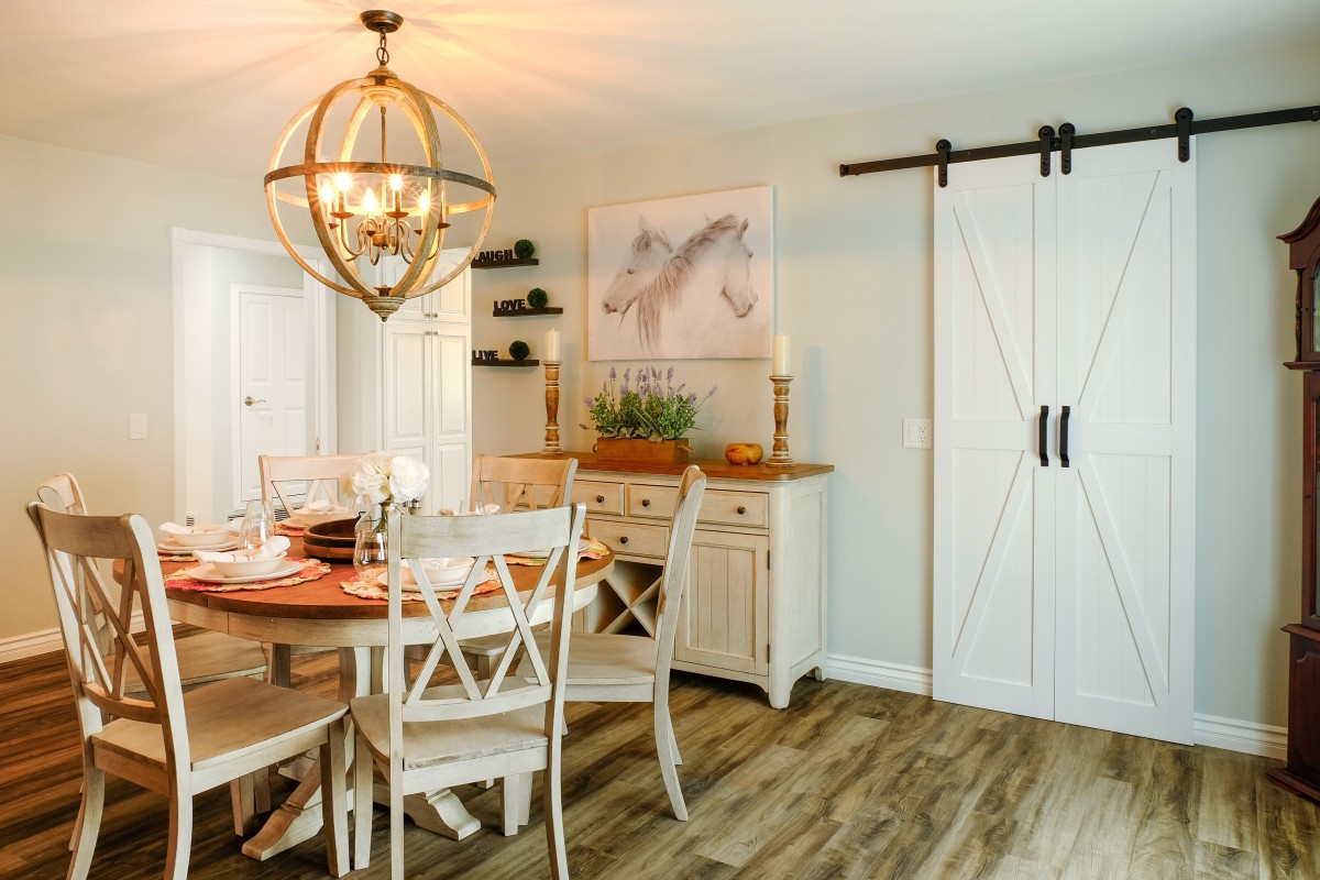 A modern farmhouse dining room with a chandelier, barn door, and wooden furniture.