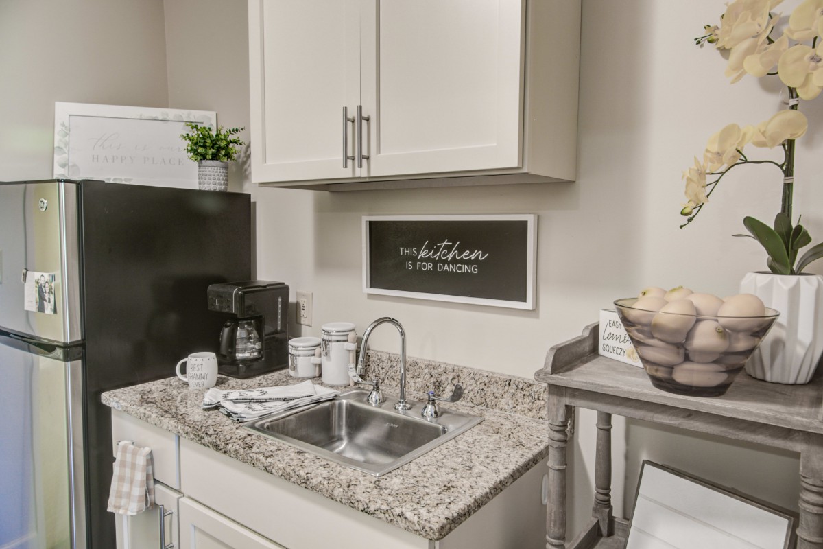 A compact kitchenette featuring a granite countertop with a sink, coffee maker, and decorative accents.