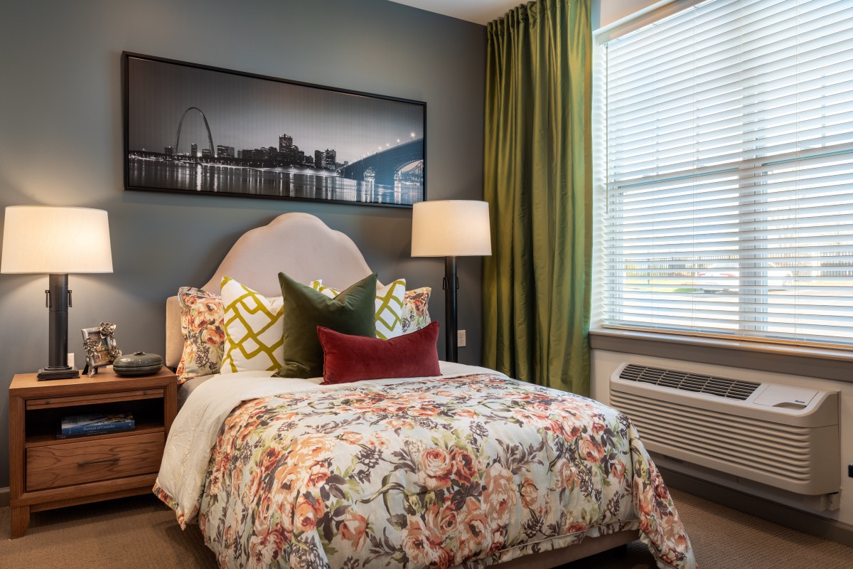 A cozy bedroom with floral bedding, decorative pillows, and a large framed artwork above the bed.