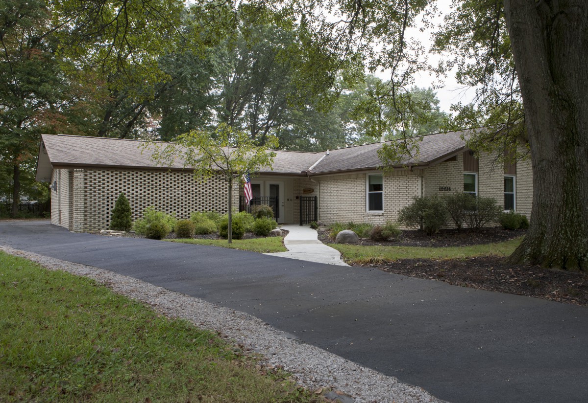 A suburban house with a long driveway surrounded by trees and landscaped greenery.