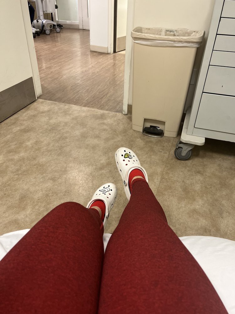 Person sitting in a hospital waiting area wearing red pants and white slippers.