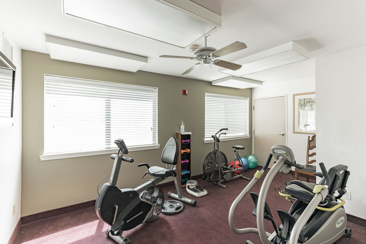 A small fitness room with various exercise equipment, including stationary bikes and a fan on the ceiling.