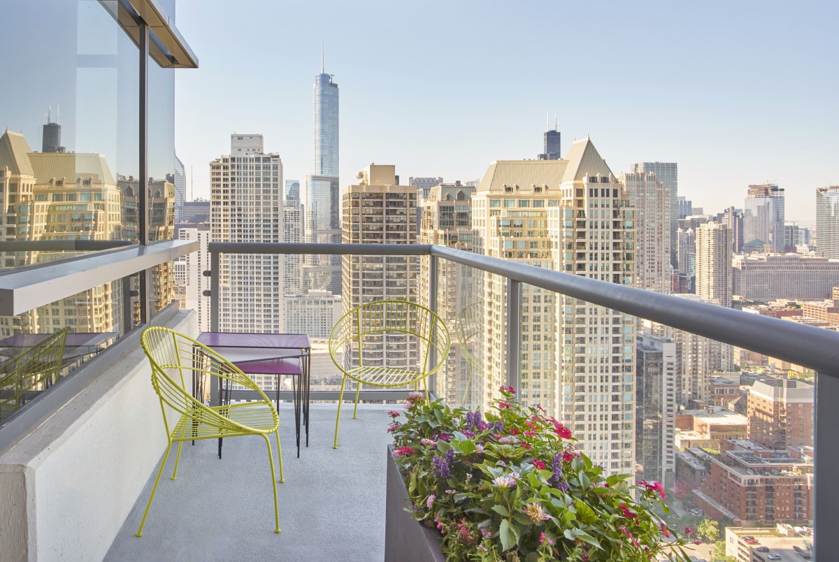 A balcony with outdoor seating overlooking a city skyline filled with skyscrapers.