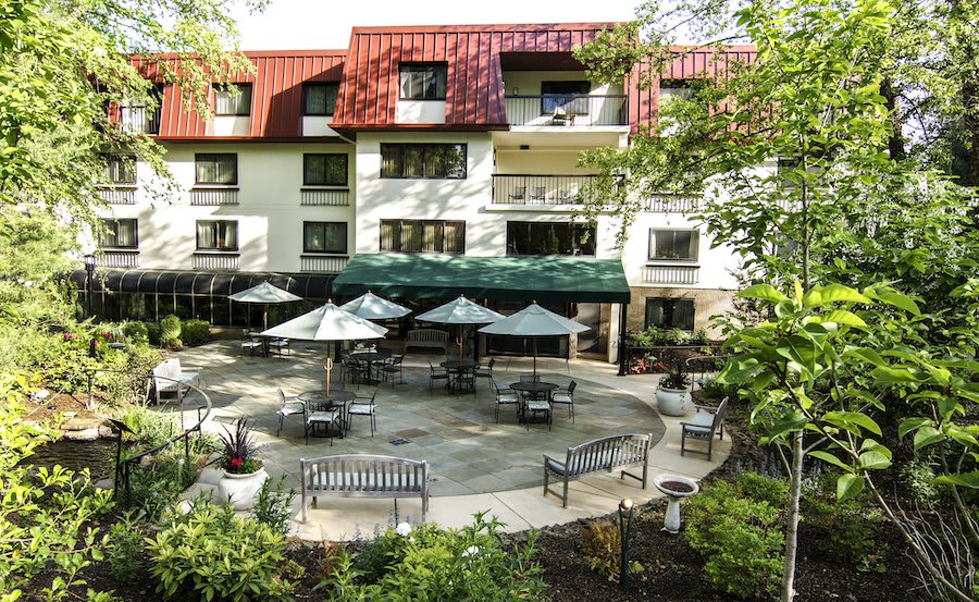 A view of a hotel building with outdoor seating on a patio surrounded by trees.