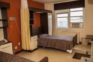 A hospital room with a single bed, large window, curtain, and air conditioning unit.