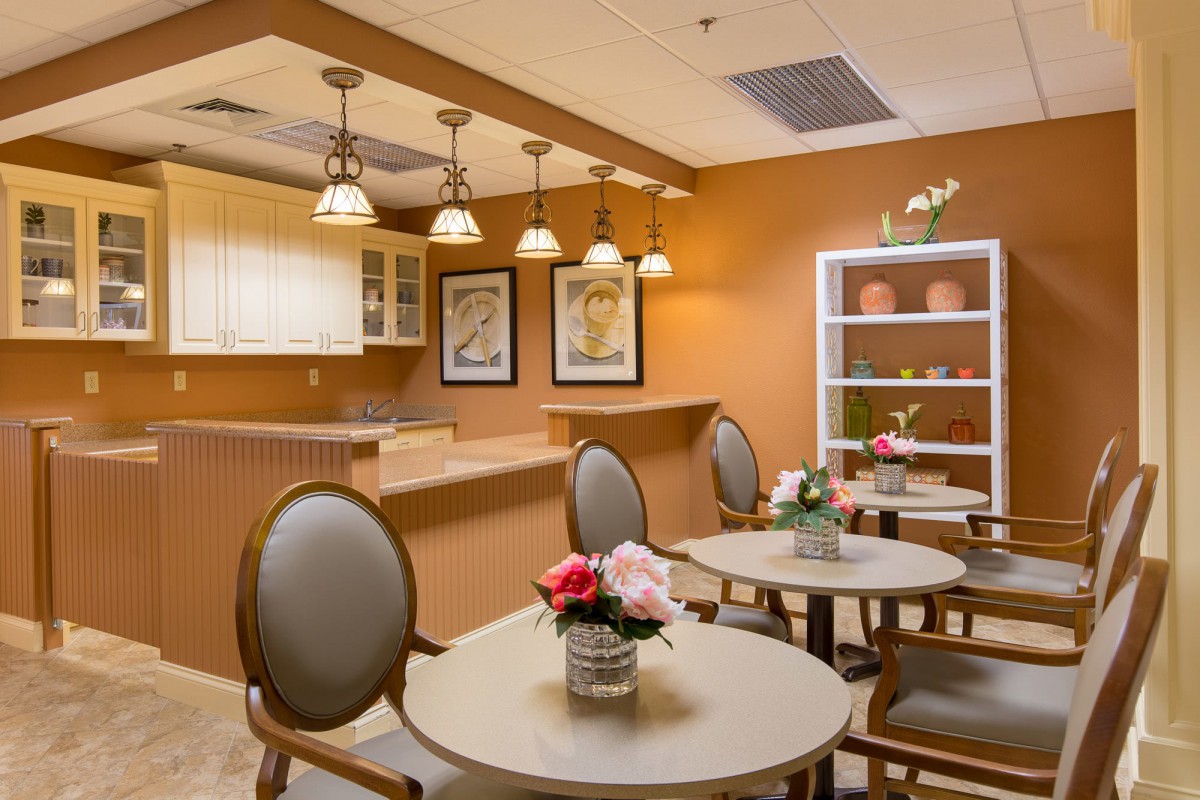 A cozy dining area with round tables, upholstered chairs, and warm lighting, featuring decorative flowers and framed artwork.