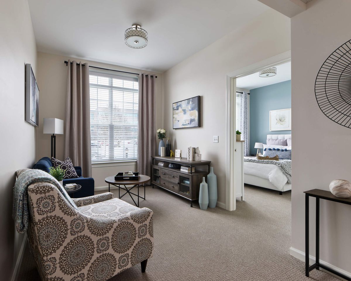 A modern living room with neutral tones and a glimpse into the bedroom.