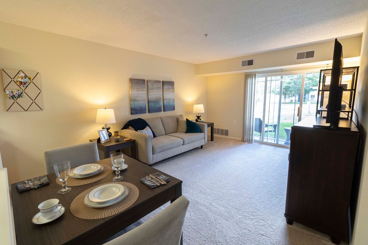 A cozy and well-lit living room with a dining area, featuring a sofa, dining table, lamps, and a sliding glass door leading to an outdoor space.