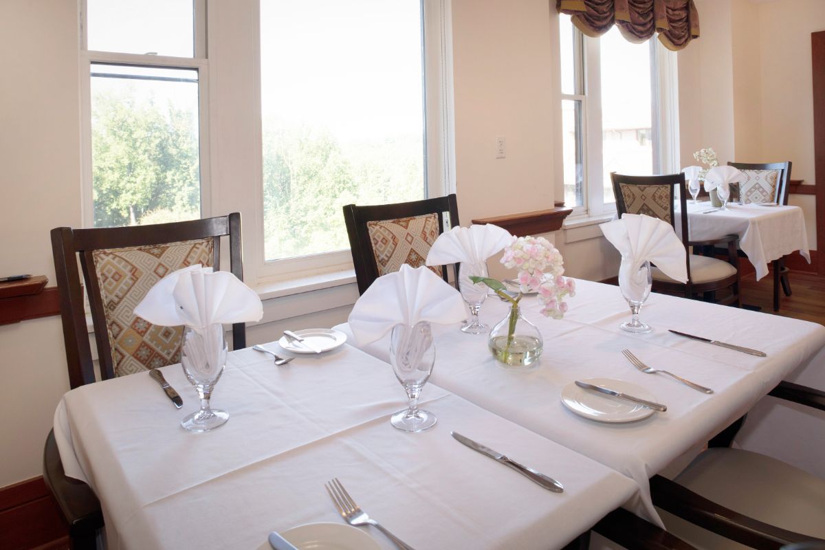An elegantly set dining table with white napkins, plates, cutlery, glasses, and a floral centerpiece.