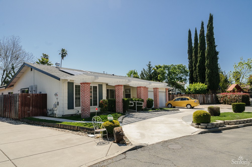 A suburban house with a driveway, front yard, and surrounding trees under a clear blue sky.