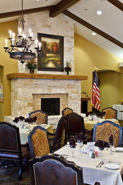 An elegantly set dining room with a stone fireplace and chandelier, featuring decorative chairs and an American flag.