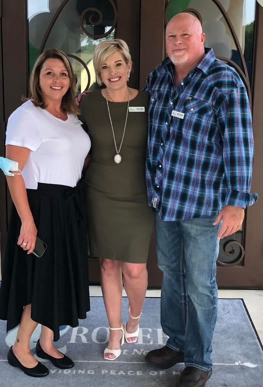 A group of three people standing together, smiling at the camera.