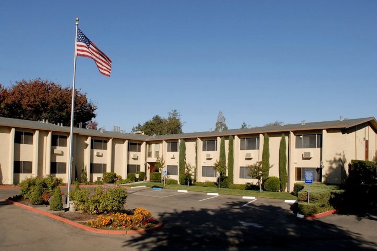 A hotel building with an American flag flying outside and a parking area in front.