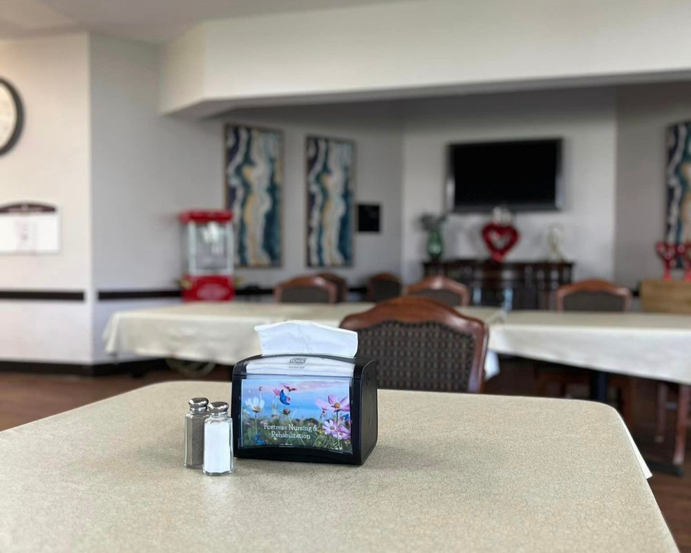 A cozy dining area with tables, chairs, and a napkin holder, featuring a television and artwork.