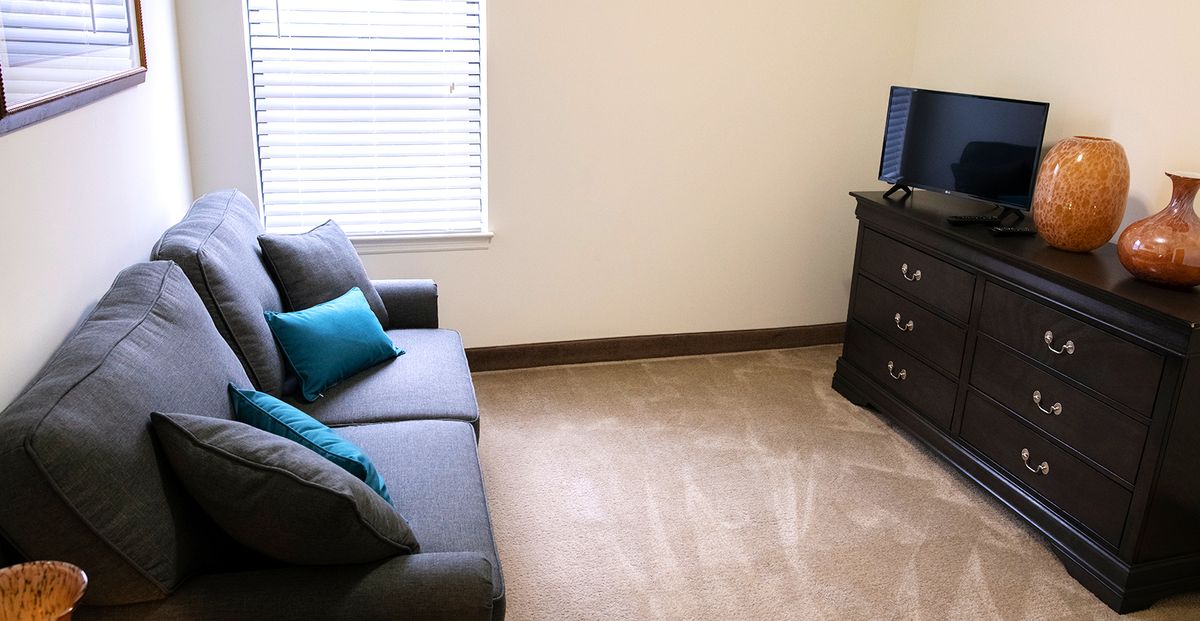 A simple living room with a gray sofa, turquoise pillows, and a television on a stand.