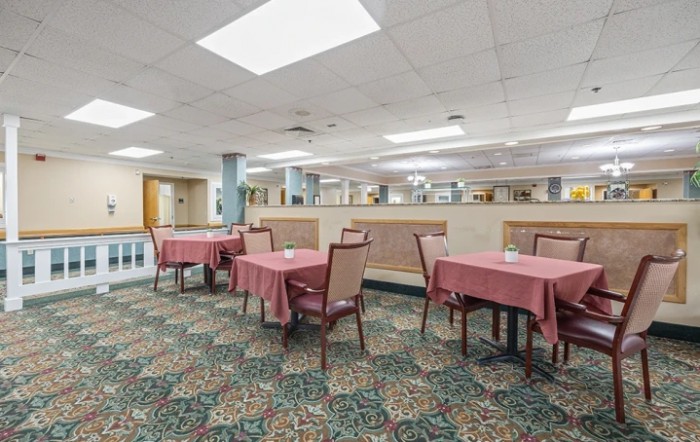 An indoor restaurant dining area with tables and chairs arranged on a carpeted floor.
