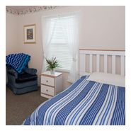 A cozy bedroom with a blue and white striped bedspread, a comfortable chair, and a bright window.