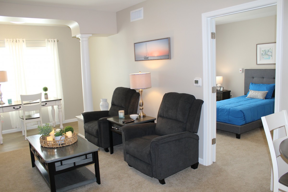 A cozy living room with two dark armchairs and a view into a bedroom.