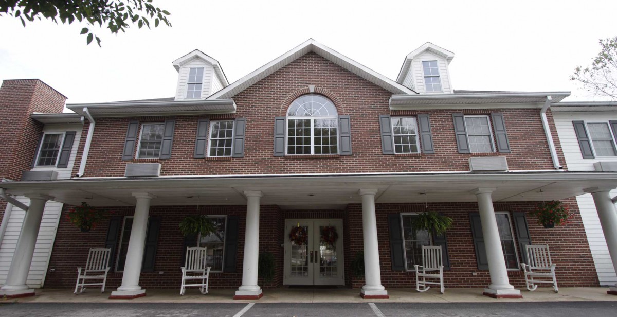 A two-story brick building with a prominent entrance, featuring columns and multiple windows.
