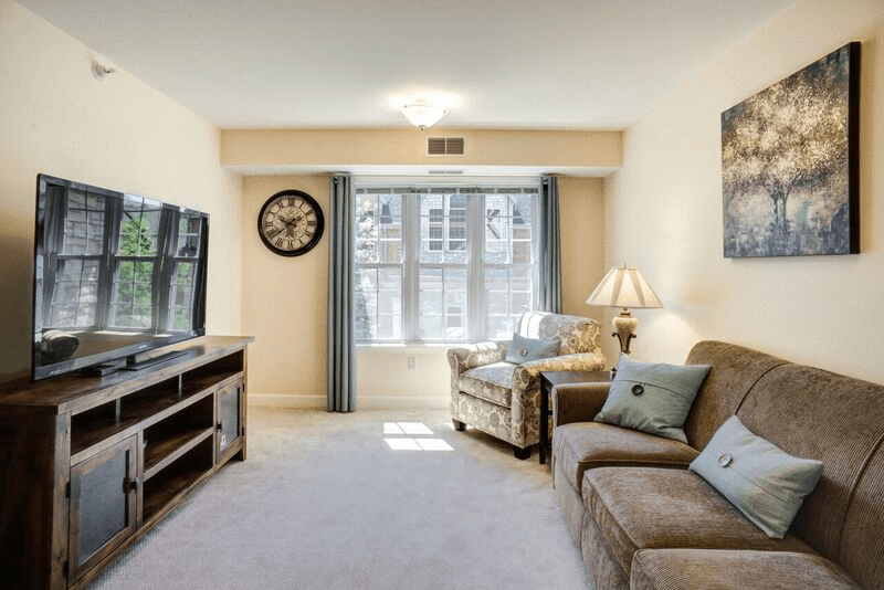 A cozy living room featuring a sofa, armchair, and television with a large window providing natural light.