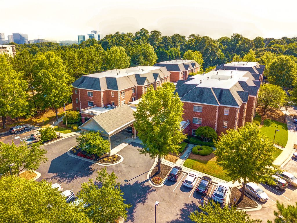 Aerial view of a suburban apartment complex surrounded by trees with a parking lot.