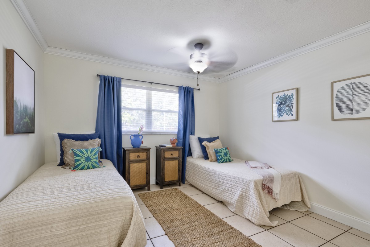 A cozy bedroom with two twin beds, blue curtains, and decorative pillows in a neutral color scheme.