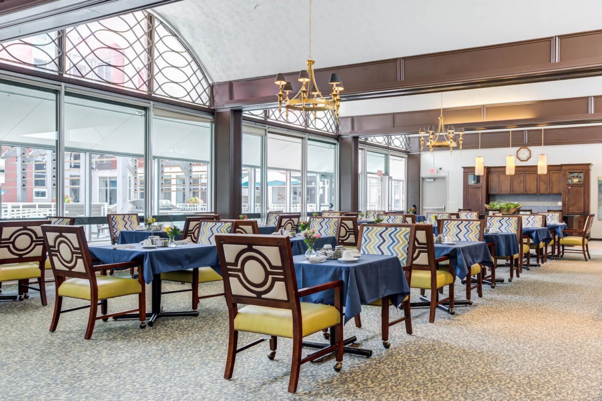 An elegant dining area with neatly arranged tables and chairs, featuring large windows and a chandelier.