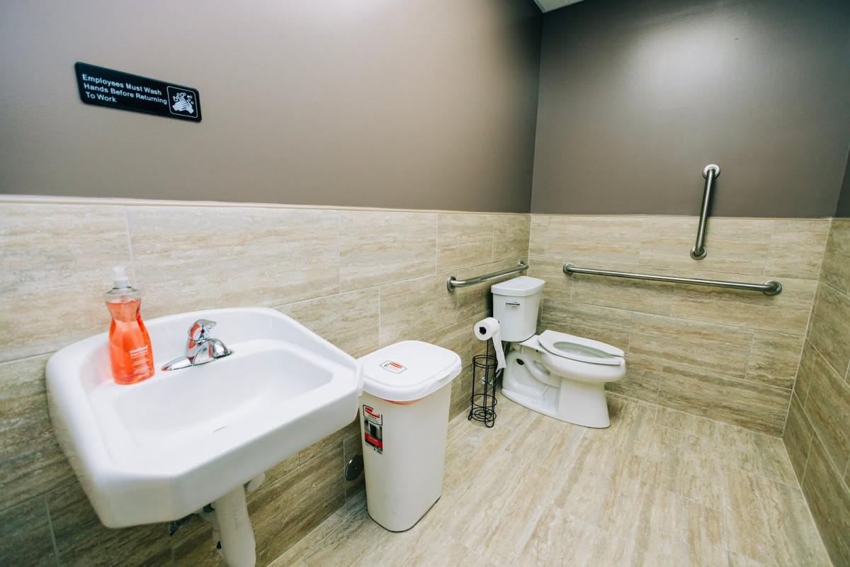 An accessible bathroom with a toilet, sink, and handrails.