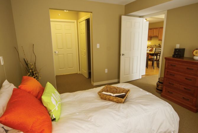 Cozy bedroom with a neatly made bed, colorful pillows, and an open door leading to a hallway.