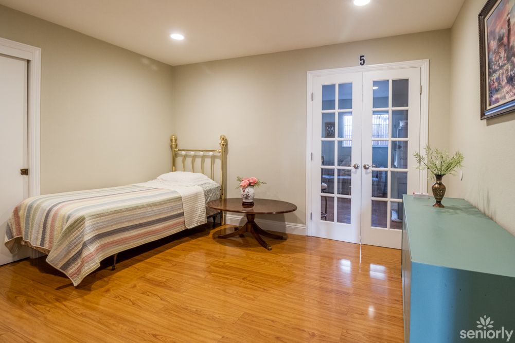 A minimalist bedroom featuring a single bed, wooden flooring, and French doors.