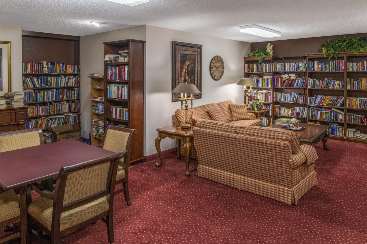 A cozy library room featuring bookshelves, a comfortable sofa, and a table with chairs.