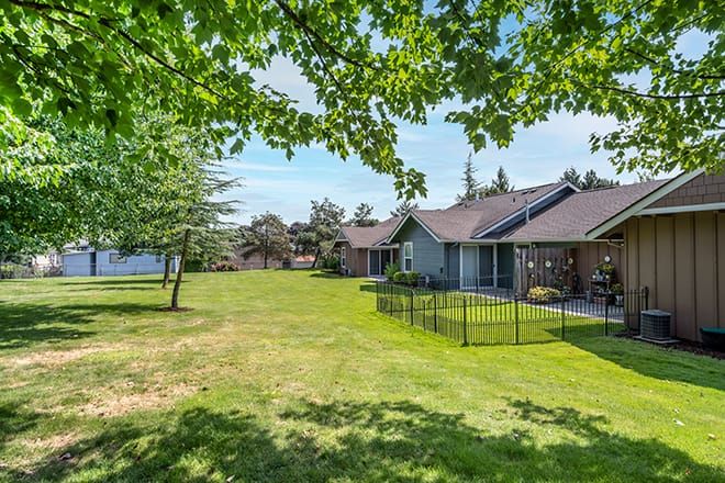 A peaceful suburban house with a spacious lawn and trees under a sunny sky.