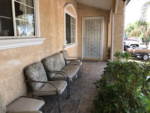 A cozy front porch with chairs and plants along a tiled walkway.