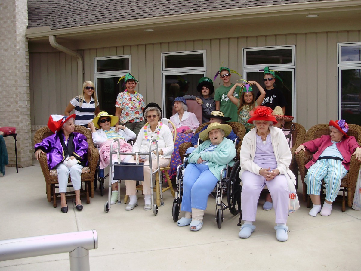 A group of elderly individuals wearing colorful hats and costumes sitting together outdoors.