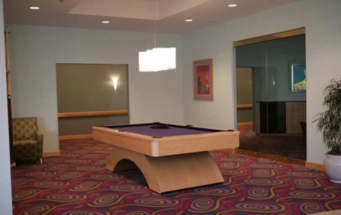 A modern room featuring a uniquely designed pool table with purple felt, complemented by patterned carpeting and contemporary lighting.